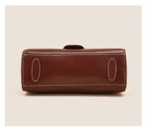 Brown leather handbag bottom detail featuring white stitching and protective feet for durability.
