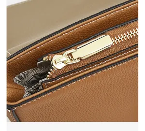 Brown genuine leather women crossbody saddle bag detail shot with gold zipper and stitching.