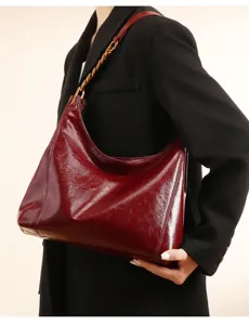 Close-up detail shot of a wine red patent leather hobo shoulder bag with gold chain.