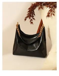 Close-up detail of black patent leather underarm shoulder bag with chunky gold chain.
