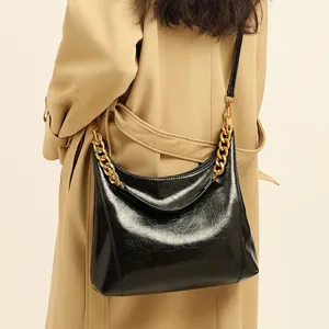 Stylish black patent leather hobo shoulder bag for women with chunky gold chain strap.