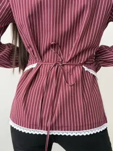 Detailed view of a striped long sleeve shirt with waist tie and lace hem for women.