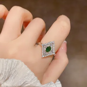 Primo piano di un anello geometrico vintage pavé di diamanti con gemma verde centrale.
