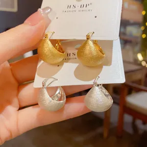Detaillierte Nahaufnahme stilvoller, tiefgebürsteter Metall-Creolen in Gold und Silber.