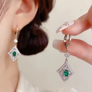 Primo piano di orecchini pendenti a rombo in argento con zirconi e pietra verde.
