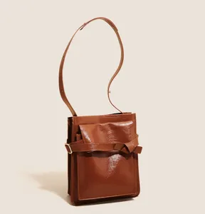 Close-up detail of the brown patent leather shoulder bag, highlighting front knot belt and strap.