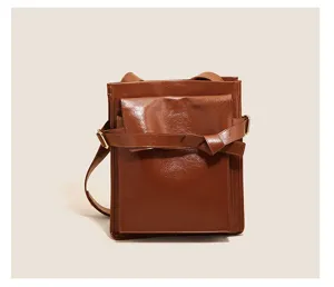 Detailed close-up of the brown glossy patent leather shoulder bag with front pocket design.