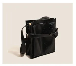 Close-up detail of the black glossy patent leather messenger shoulder bag with strap buckle.