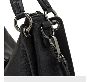 Close-up detail shot of black leather handbag featuring metallic hardware rings and hooks.