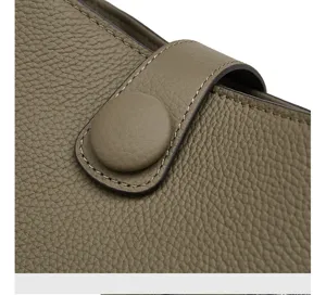 Gros plan sur la texture en cuir de vachette véritable, finitions et bouton pression.