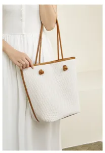 Detail shot of the stylish woven tote shoulder bag with brown leather trim and cute knot handle accents.