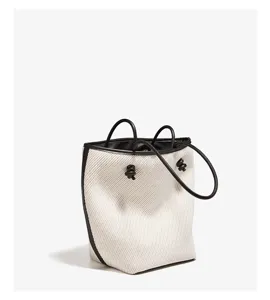 Elegant canvas bucket bag with black leather trim, top handles and chic knotted drawstring.