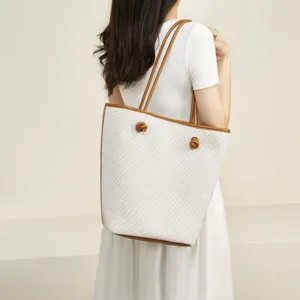Elegant white woven tote bag with brown leather handles and chic knot details for women.