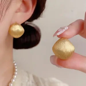 Detailaufnahme französischer goldener geometrischer Ohrringe mit feiner Drahtziehtextur.