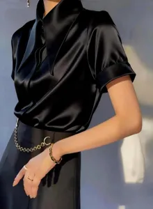 Close-up detail of women's black satin short-sleeve shirt with chic collar and chain.