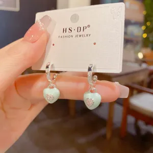 Close-up detail of light green enamel heart drop earrings with sparkling rhinestone.