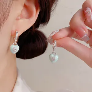 Close-up detail of stylish mint green enamel heart drop earrings with glittering crystal stones.