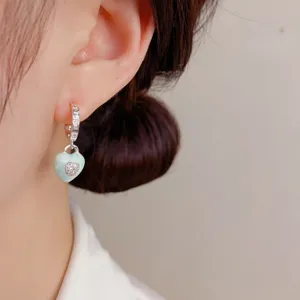 Close-up of silver enamel heart hoop earrings with shiny green drop oil and tiny pave diamonds.