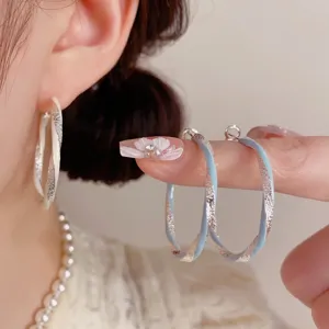 Dettaglio orecchini a cerchio torsi con finitura glitterata, elegante stile di indossarli al dito.