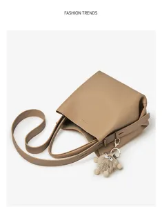 Beige leather bucket bag detail featuring long shoulder strap and cute plush ball charm.