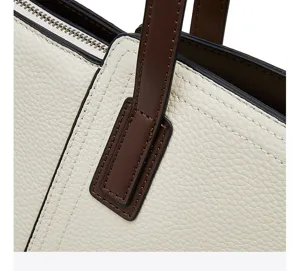 Close-up detail of cream white pebbled leather tote bag with brown straps and fine stitching.