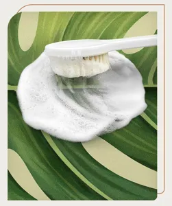 Detailed view of a long-handled bath brush with rich foam on a green leaf pattern mat.