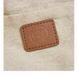 Detailed shot of woven straw bag with brown leather patch logo, casual summer beach accessory.