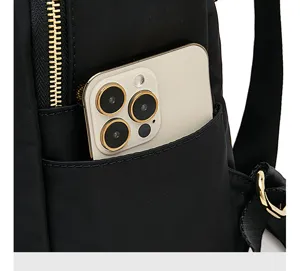 Primo piano della tasca anteriore dello zaino in nylon nero con smartphone e dettagli dorati.