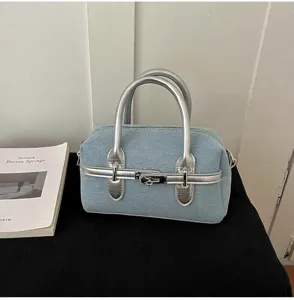 Stylish denim bowling handbag for women with silver top handles and front metal lock design.
