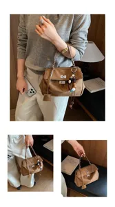 Nahaufnahme einer braunen Wildlederhandtasche mit Metallverschluss und Perlenanhänger.