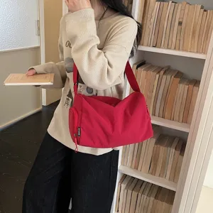 Detailopname van een rode canvas crossbodytas met ritvak en verstelbare schouderband.