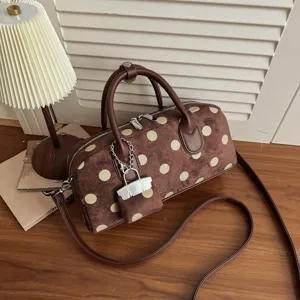 Detailed view of brown polka dot handbag showing soft suede and stylish metal chain charm.