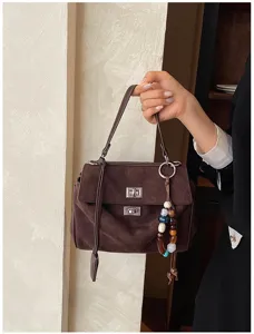 Braune Wildleder Handtasche Detailansicht mit stilvollem Metallschloss und Perlen Anhänger.
