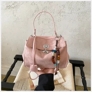 Rosa Wildleder Handtasche Detail mit elegantem metallischem Drehverschluss und Perlenanhänger.