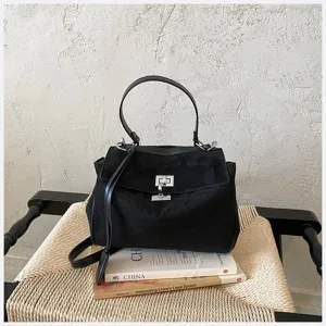 Detailansicht der schwarzen Wildleder Handtasche mit Metallverschluss auf geflochtenem Hocker