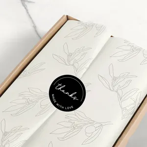 Detail view of black round thank you sealing sticker on elegant botanical tissue paper packaging box.