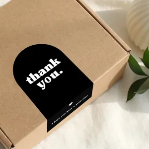 Close-up of minimalist black arched thank you sticker on brown gift box packaging.