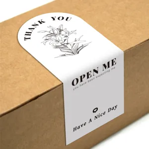 Detalle de pegatina de agradecimiento floral con elegante diseño de flores en caja de cartón.
