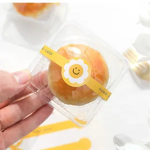 Klare Kunststoff-Verpackungsbox mit gelbem Smiley-Versiegelungsaufkleber für köstliches Gebäck.