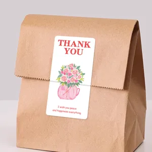 Vista detallada de pegatina rosa floral de agradecimiento aplicada en bolsa de papel kraft.