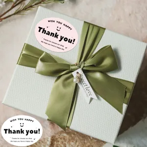 Thank you sticker gift box packaging detail shot with elegant green ribbon and decorative tag.