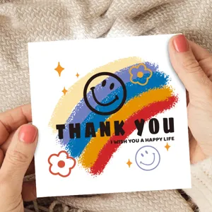 Primer plano de una tarjeta de felicitación cuadrada con diseño de arcoíris y caras sonrientes.