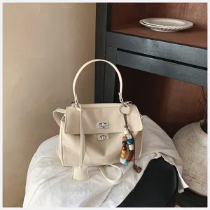 Schicke beigefarbene Henkeltasche mit Drehverschluss und stylischem Perlenanhänger.
