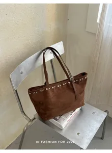 Détail de sac cabas en suédine marron, ornements de rivets élégants, sac porté épaule spacieux.