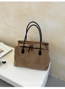 Detail van bruine suède tote tas met dubbele zwarte handvatten en veilige ritssluiting.