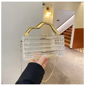 Dettaglio borsa da sera in acrilico trasparente con manico dorato e catena elegante.