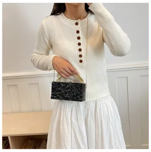 Vista dettagliata della elegante pochette rigida nera testurizzata con catena dorata in scena.