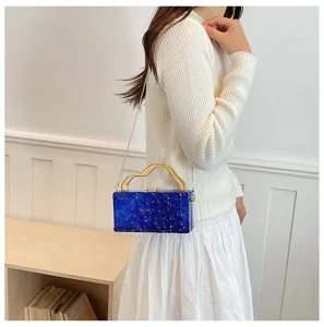 Elegante borsa pochette rigida in resina blu con manico dorato e tracolla a catena.
