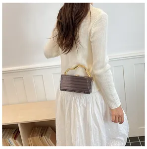 Dettaglio borsa a mano in acrilico trasparente con manico metallico ondulato e catena elegante.