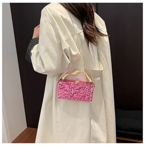 Elegante borsa da sera in acrilico rosa con manico dorato e tracolla a catena.